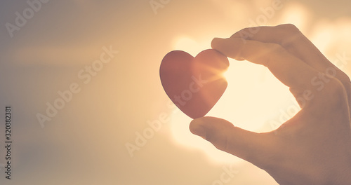 Hand holding up heart with rays of sunshine shinning through. 