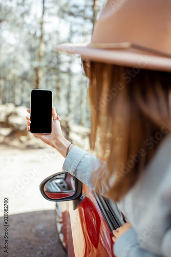 Woman traveling by car in the forest, leaning out of the car window and photographing with a smart phone. Phone with empty screen to copy paste