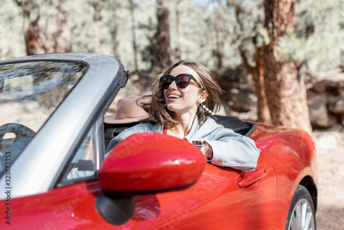 Portrait of a happy carefree woman driving convertible red car while traveling in the forest © rh2010