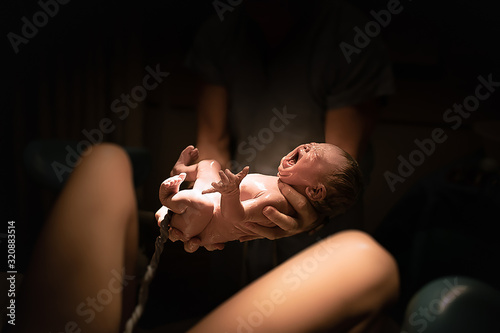 Doctor holding newborn baby girl moments out of mothers womb. New life, giving birth, concept.  photo