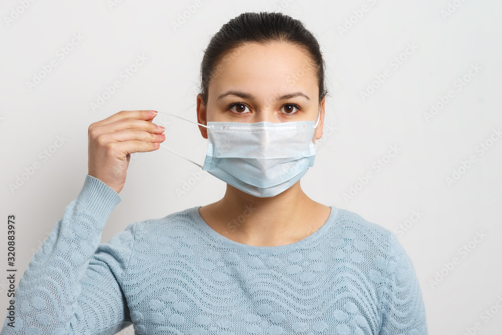 Studio portrait of young woman wearing a face mask, looking at camera, close up, isolated on gray background. Flu epidemic, dust allergy, protection against virus