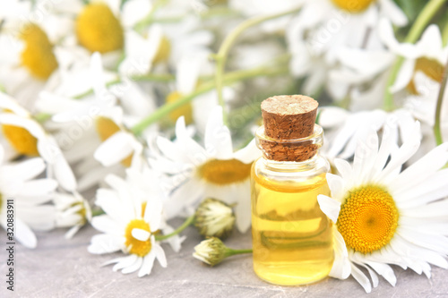 Essential oils on medicinal chamomile flowers and herbs background, selective focus, shallow DOF, toned 