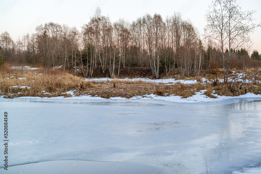 Pond covered with ice with reflections of spring sky and trees Pond covered with ice with reflections of spring sky and trees