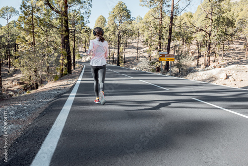 Wallpaper Mural Young woman in sportswear jogging on the beautiful mountain road in the forest, wide view from the backside Torontodigital.ca