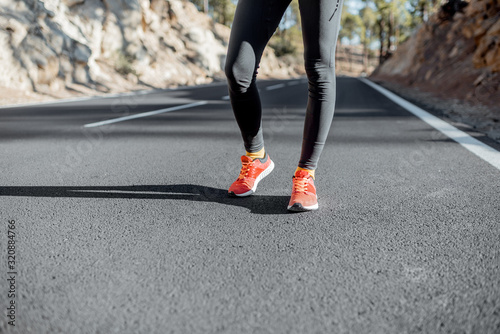 Sports woman in running shoes standing on the asphalt mountain road, close-up on sneakers