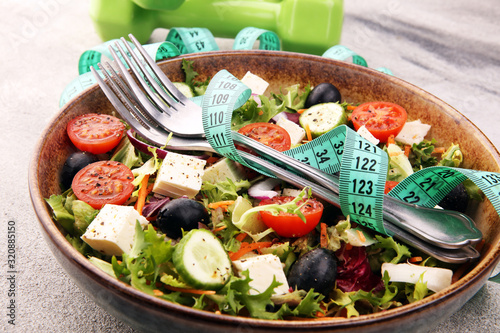 Authentic fresh salad in a stone cup with dumbbells excercise equipment, measuring tape on table. healthy lifestyles, good health Concept with fresh ingredients