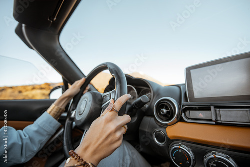 Woman driving car on the desert road, close-up view focused on the steering wheel and hands