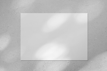 Empty white horizontal rectangle poster or business card mockup with diagonal dappled light spots on gray concrete wall. Flat lay, top view. For advertising, brand design, stationery presentation.