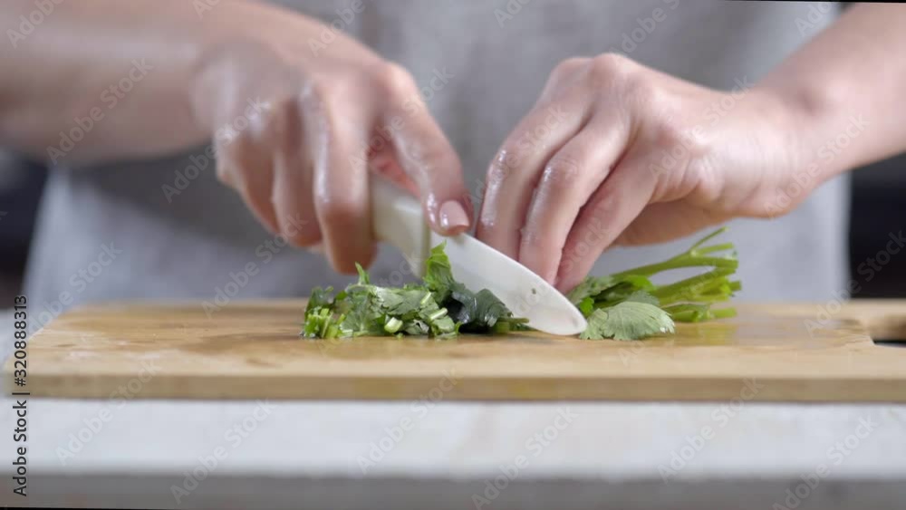Hands of woman cooking and cutting parsley with a knife on the kitchen counter close up