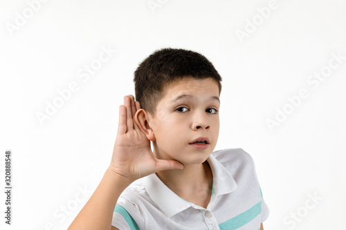 happy little child boy in striped t-shirt making hearing gesture on white background. facial expression. kid with hand over ear listening gossip.