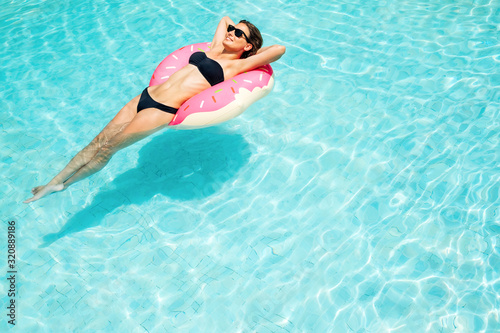 Enjoying suntan woman in black bikini on the inflatable mattress in the swimming pool. Summer vacation concept