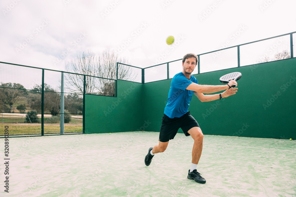 Young man playing paddle tennis on a green court, wearing a blue t-shirt.Sports concept.Copy space