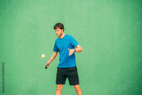 Young man playing paddle tennis on a green court, wearing a blue t-shirt.Sports concept.Copy space © JAVIER LARRAONDO