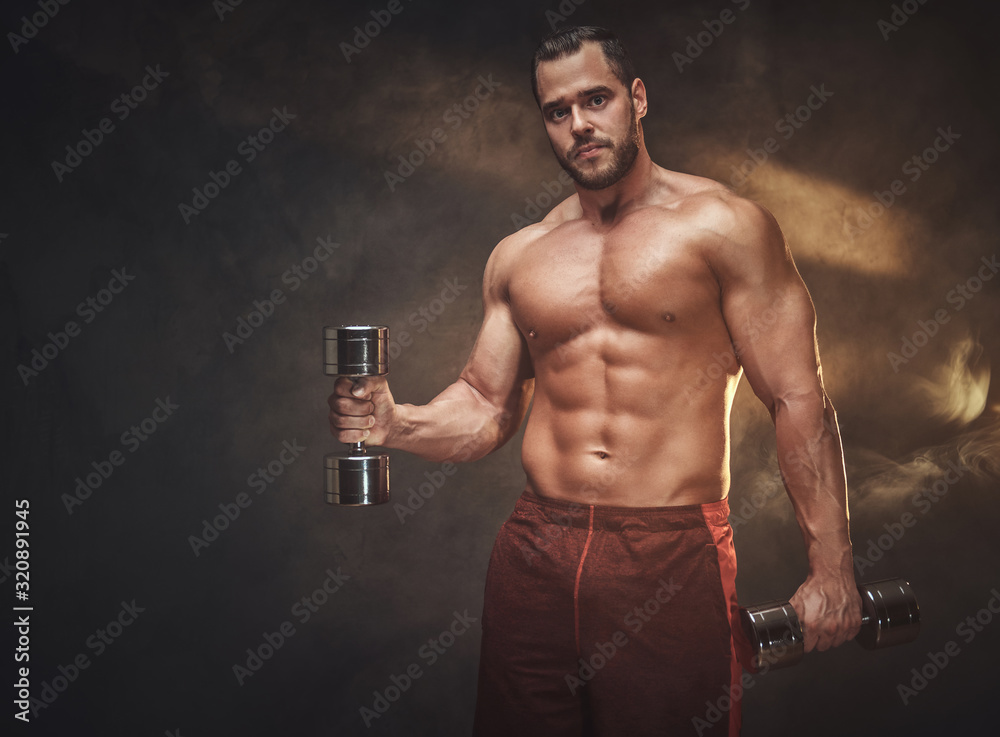 Young handsome bodybuilder is posing for photographer with dumbbells. Young handsome bodybuilder is posing for photographer with dumbbells.