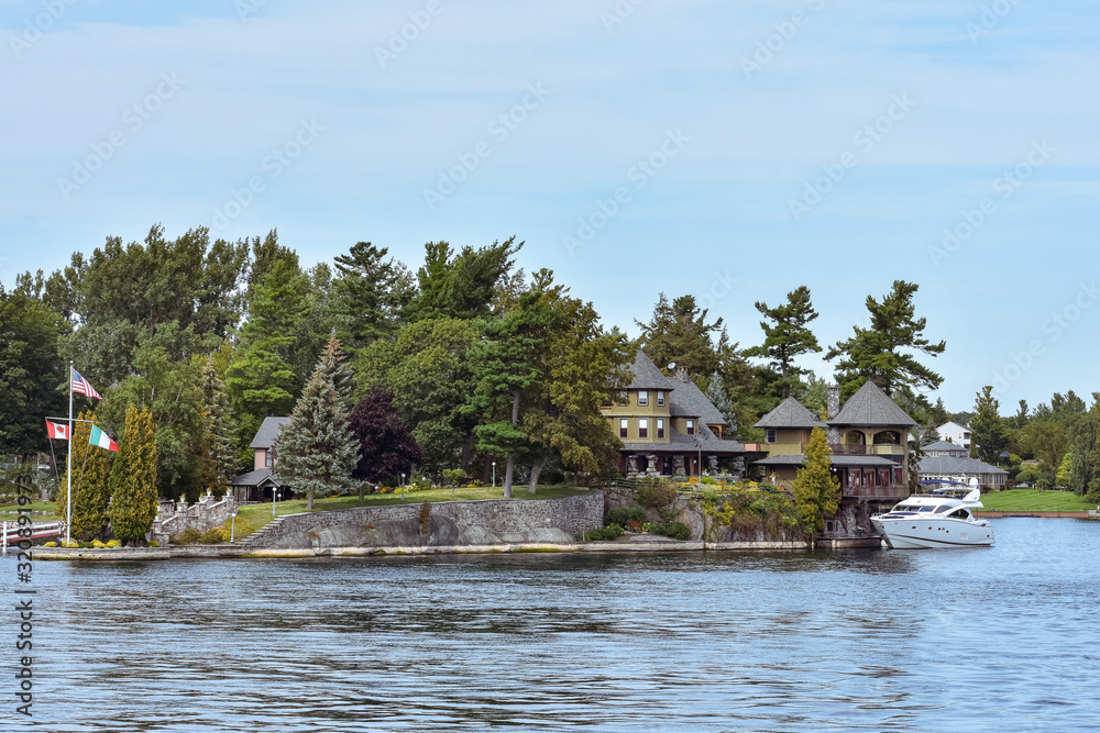 Building in a grassy area on the coast of a lake during daytime, and surrounded by trees. Yacht parked in the lakeside harbor. Real state concept. Thousands Islands. Ontario, Canada
