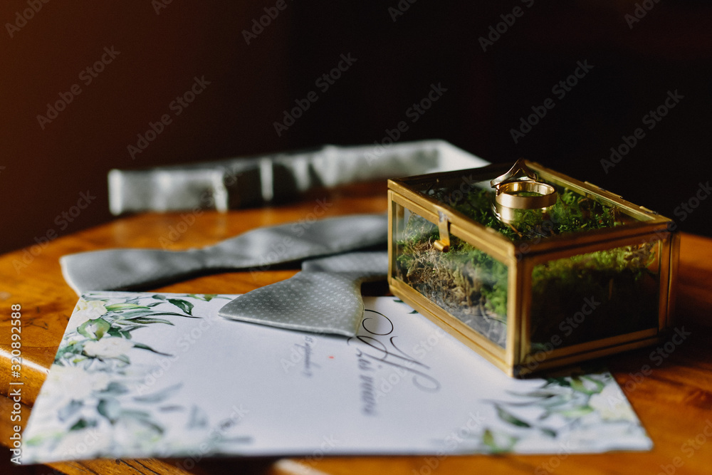 Untied bowtie and wedding rings in box with micro moss and wedding invitations on the wooden table Untied bowtie and wedding rings in box with micro moss and wedding invitations on the wooden table