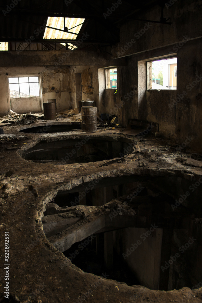 Fototapeta premium Large holes in the wooden floor of the top floor of an abandoned factory with rusty drums, dirt and debris.