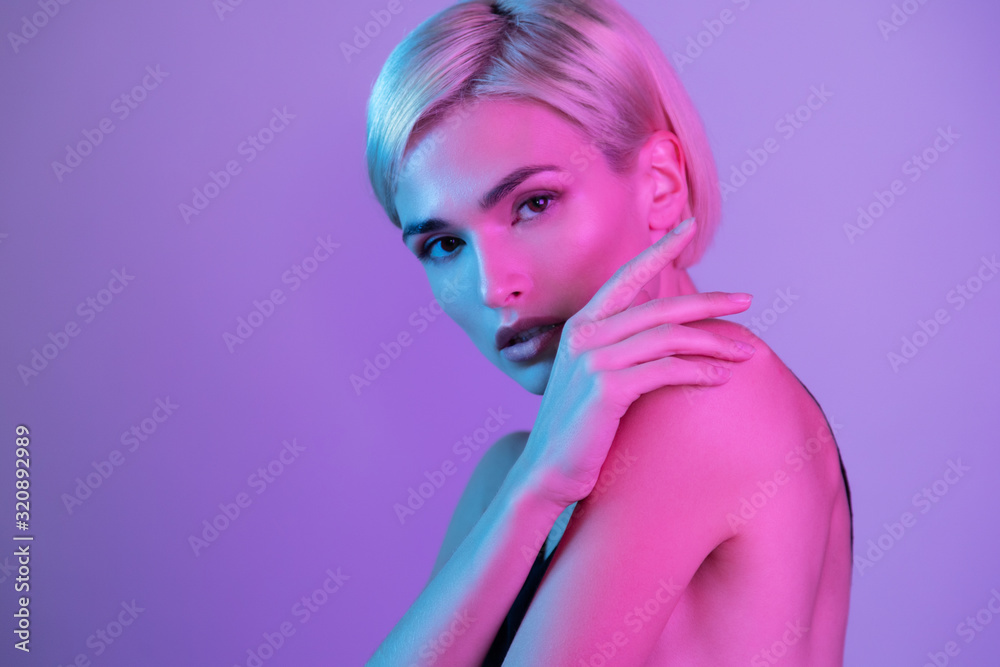 Beautiful awesome woman covering naked shoulders with hands standing sideways and looking at camera under neon uv light. Studio fashion beauty headshot portrait Beautiful awesome woman covering naked shoulders with hands standing sideways and looking at camera under neon uv light. Studio fashion beauty headshot portrait