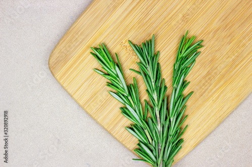 Top view of bright fresh green rosemary branches, twigs and leaves on a wooden board on light background.