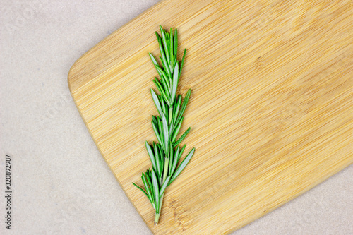 Top view of bright fresh green rosemary branches, twigs and leaves on a wooden board on light background.