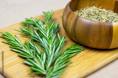 Bright fresh green and dried rosemary branches, twigs and leaves in a wooden bowl and board on light background.