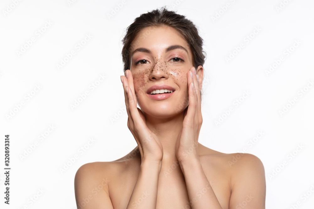 Beautiful woman with perfect skin applying exfoliating coffee scrub on nose and cheeks studio portrait on white copy space. Beauty facial peeling procedure for soft purifying and skincare Beautiful woman with perfect skin applying exfoliating coffee scrub on nose and cheeks studio portrait on white copy space. Beauty facial peeling procedure for soft purifying and skincare