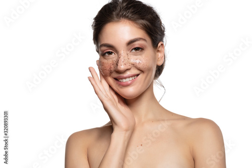 Smiling satisfied woman with coffee scrub on face studio portrait isolated on white copy space. Face skin care, exfoliating and peeling. Natural beauty product for scrubbing facial treatment mask photo