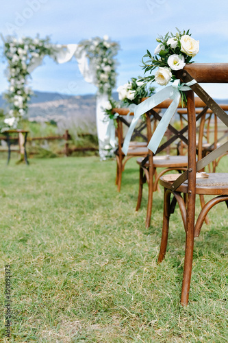 Brown chiavari chairs decorated with white eustomas on the grass and the decorated wedding archway on the background photo