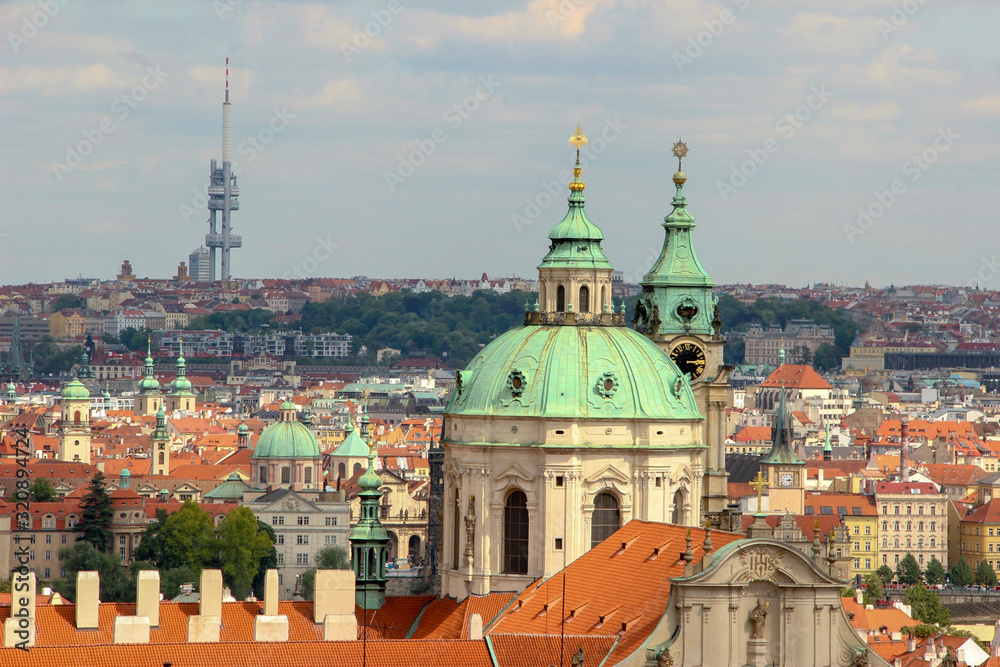 Dome and clock tower of old baroque St. Nicholas Church (Malá Strana) of 18th century. Roofs of houses and buildings of Prague. Skyline with a television tower.