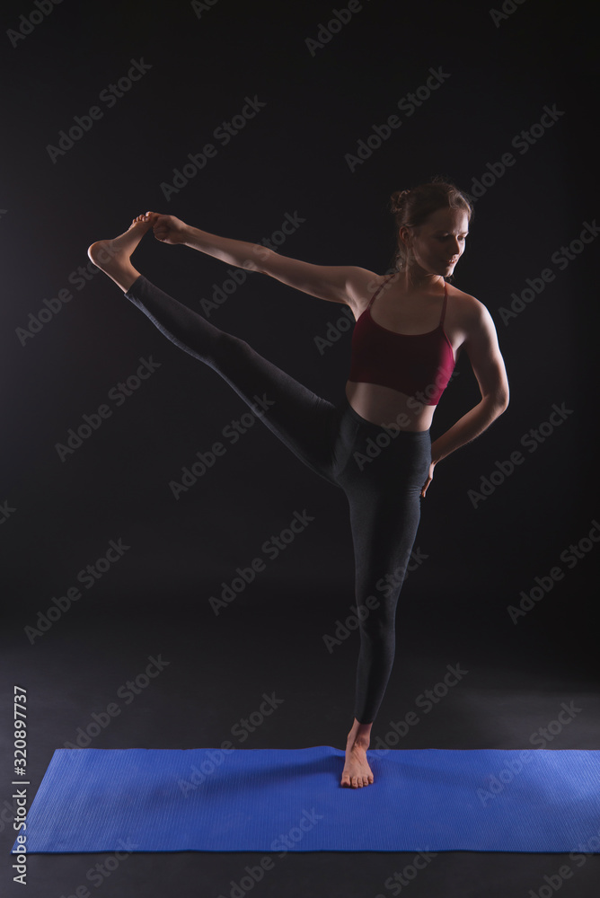 Gorgeous woman practicing yoga (Standing Hand to Toe Preparation) in black studio.
