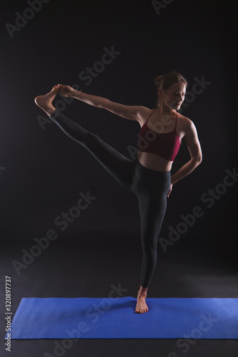 Gorgeous woman practicing yoga  Standing Hand to Toe Preparation  in black studio.