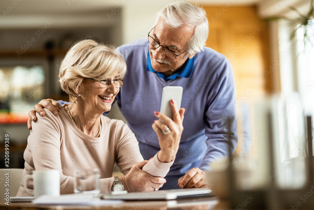 Happy senior woman using cell phone with her husband at home. Happy senior woman using cell phone with her husband at home.