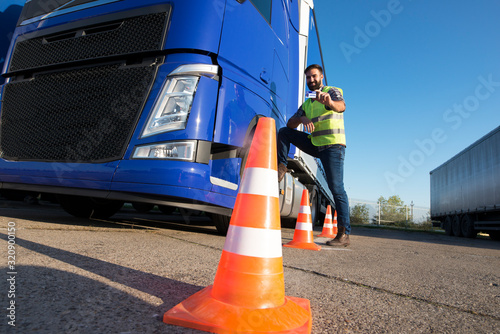 Truck driving school. Shot of bearded man learning how to drive truck at driving schools. Truck driver candidate training for driving license. Standing by the traffic cone in reflective vest.