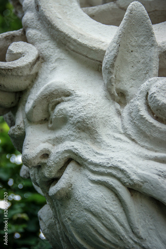 Face made in stone of bearded man with pointy ears. Detail of an ancient base. photo