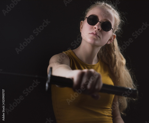 A beautiful young girl with a Japanese sword in her hands, a blonde in round dark glasses with a cold weapon in her hands