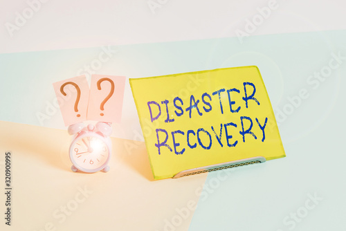 Word writing text Disaster Recovery. Business photo showcasing helping showing affected by a serious damaging event Mini size alarm clock beside a Paper sheet placed tilted on pastel backdrop