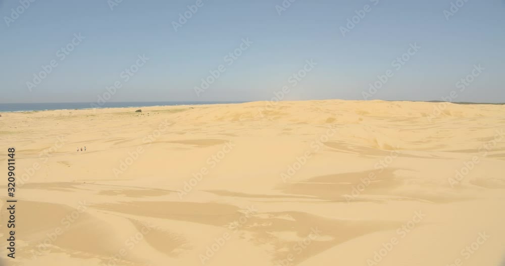 A group of three young females walking in the distance along the natural forming sand dunes at Anna Bay in Port Stephens, New South Wales, Australia A group of three young females walking in the distance along the natural forming sand dunes at Anna Bay in Port Stephens, New South Wales, Australia