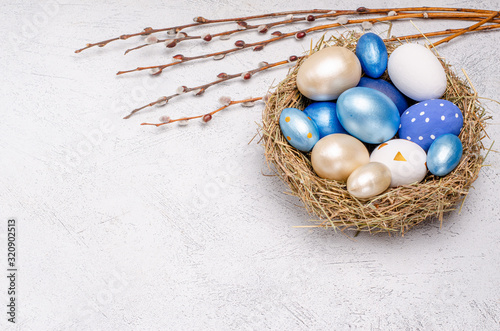 Easter eggs in blue tones in a nest of straw with willow branches on a gray background with place for copy space