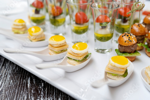 Toasts with fried eggs, cheese and salad. In the background are mini burgers, canapes with pesto sauce.