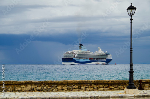 Modern cruiseship or cruise ship liner Marella Explorer 2 anchoring at sea seen from seaside walk way with lantern and stone wall during cruising the Mediterranean to the Greek Isles photo