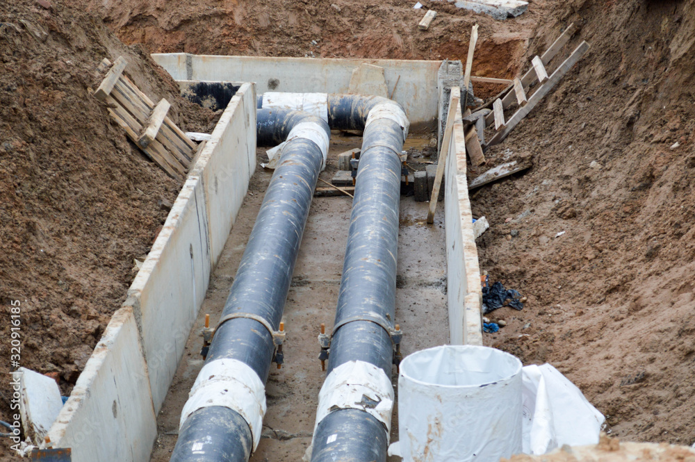 Large black metal and plastic water pipes for hot and cold water at a construction site during a repair in a new neighborhood under the ground Large black metal and plastic water pipes for hot and cold water at a construction site during a repair in a new neighborhood under the ground