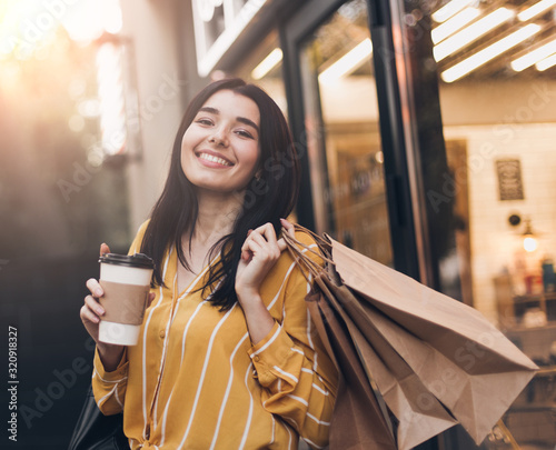 Young pretty woman in yellow skirt with shopping bags, cup of black coffee and smartphone