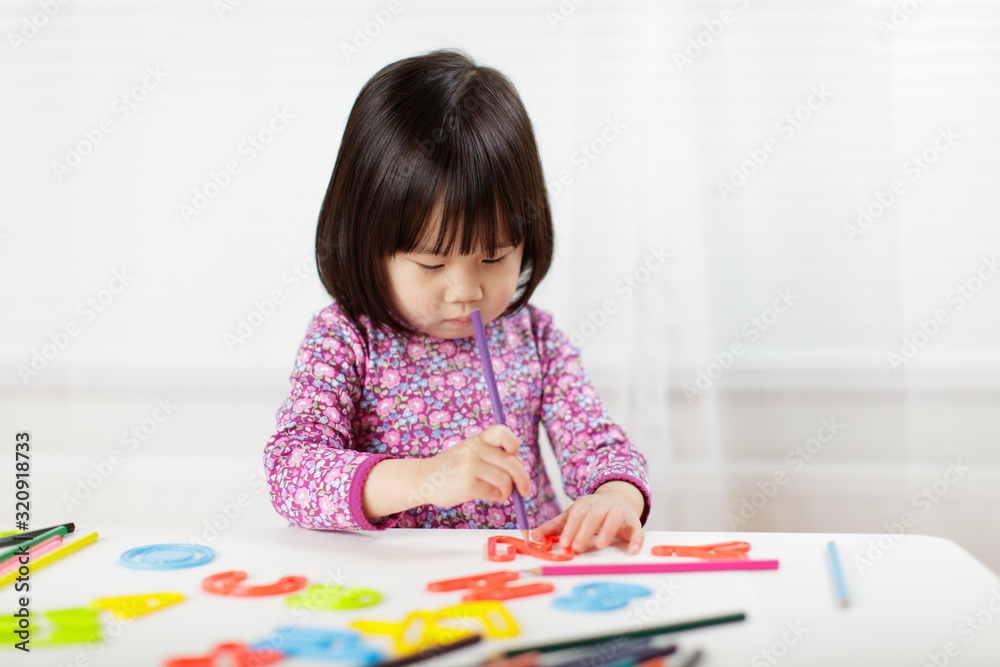toddler girl practice writing letters on white paper against white background toddler girl practice writing letters on white paper against white background