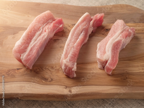 Three raw uncooked pork belly portions on a wooden cutting board. Selective focus.