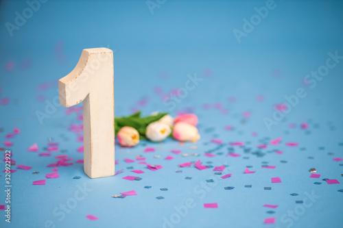 White wooden unit on a background of confetti and sparkles. First birthday.