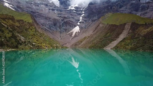 Aerial, low, drone shot tilting over crystal clear, turquoise water of lake Humantay, in the Andes mountains, on a overcast day, in Peru, South America photo