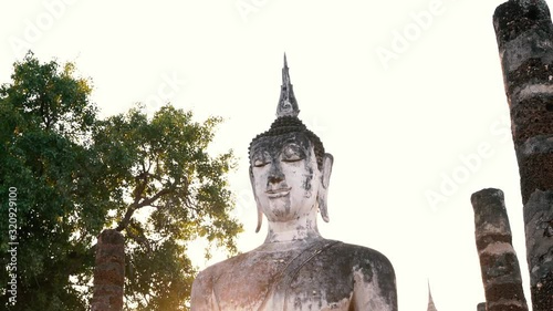 Sculpture standing buddha image of Wat Mahathat in the National Park of Sukhothai in Thailand at sunset. Travel to Asia and holidays concept. Buddhist religion, ancient art and asian heritage culture.