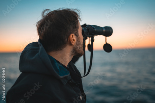 Middle-aged man with white skin is in a state of see with binoculars towards the sea.
