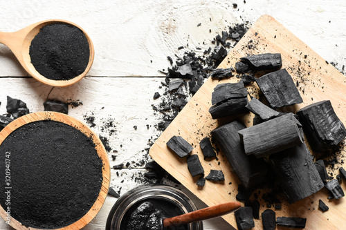 Black charcoal powder for facial mask and scrub, placed on a white wooden table, health and beauty concept. photo