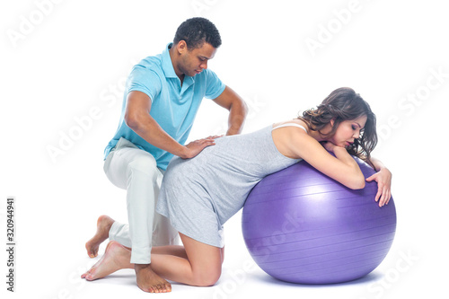 A young black man helps his white wife with birth pain with a ball. Partnered birth, partnered delivery. Isolated white background.
